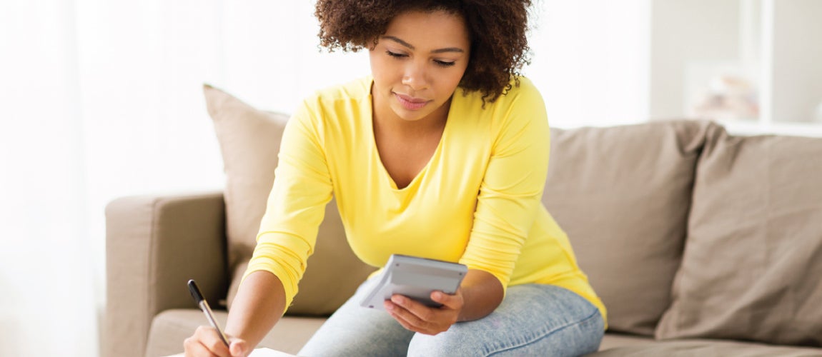 woman on a couch writing on a pad of paper