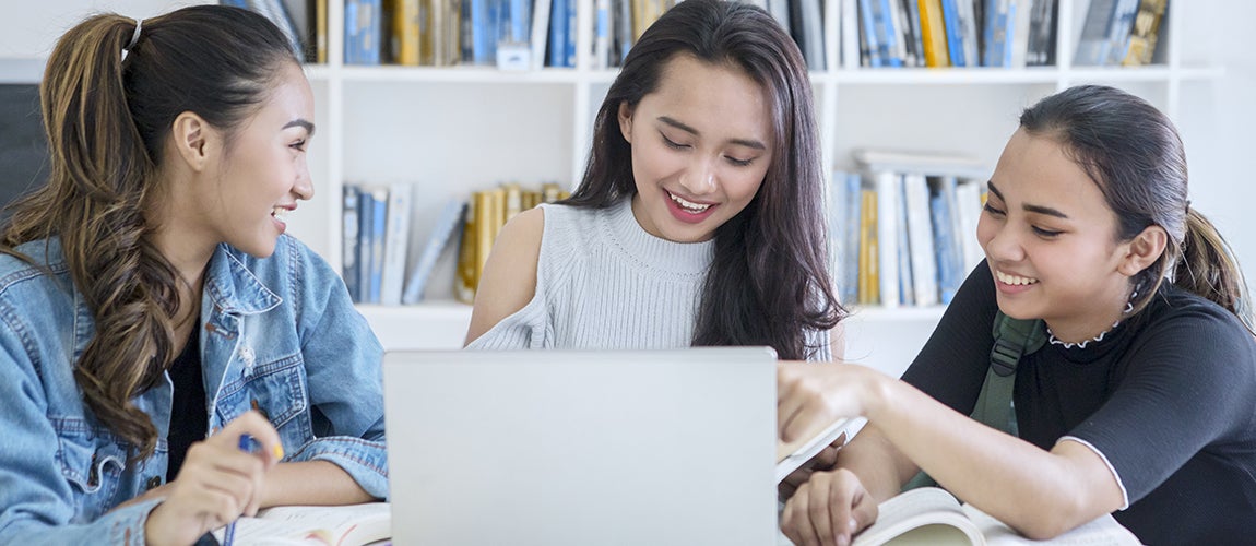 Three teenagers look at a computer and learn about finances and saving money.