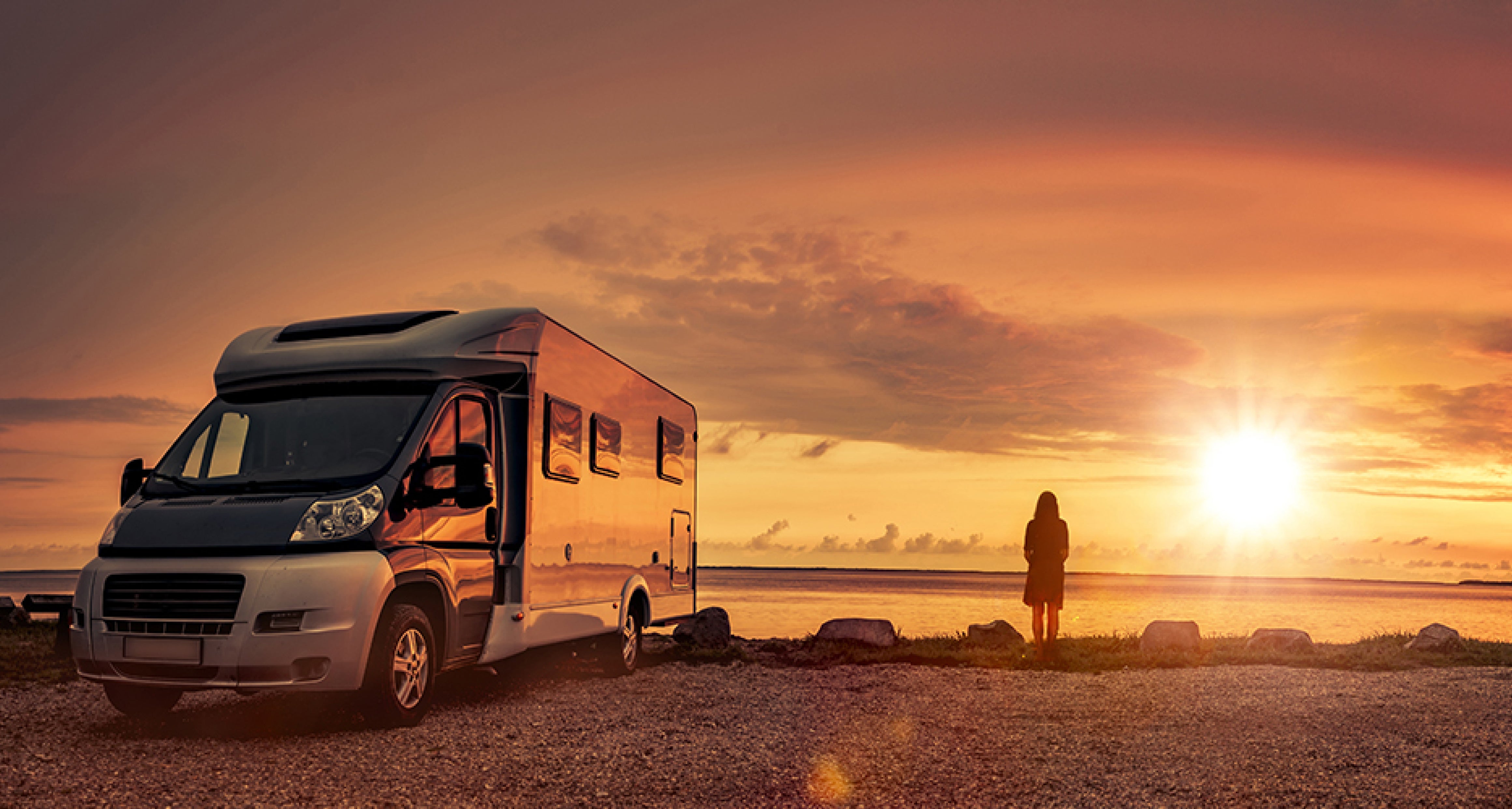 Woman watches sunset over ocean standing next to an RV she financed.