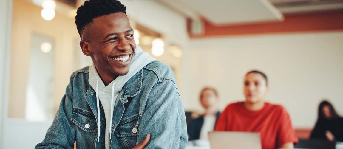  Male student sitting in a classroom considering student loans and learning how to refinance student loans.