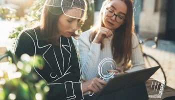 two women on patio using laptop