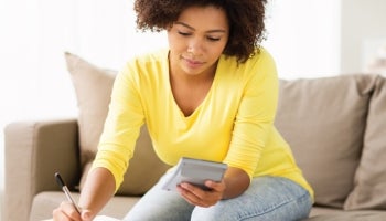 woman on a couch writing on a pad of paper