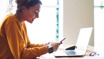 College student using cell phone and computer to examine student loans