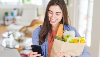 Young adult shopping for groceries while checking her bank account balance on her phone’s mobile banking app.