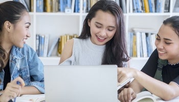 Three teenagers look at a computer and learn about finances and saving money.