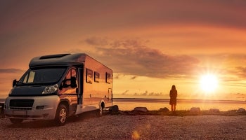 Woman watches sunset over ocean standing next to an RV she financed.