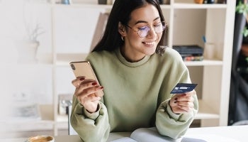 Young woman who is happy about receiving new credit card activates it from her mobile phone
