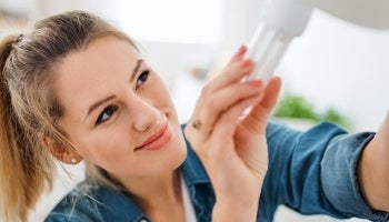Woman smiling while replacing light fixture with energy efficient light bulb