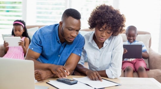 couple doing finances while children use mobile devices in background