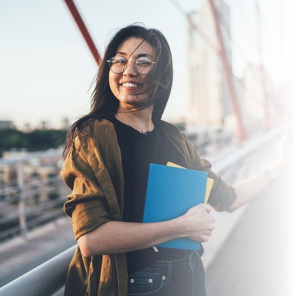 woman on bridge holding notebooks